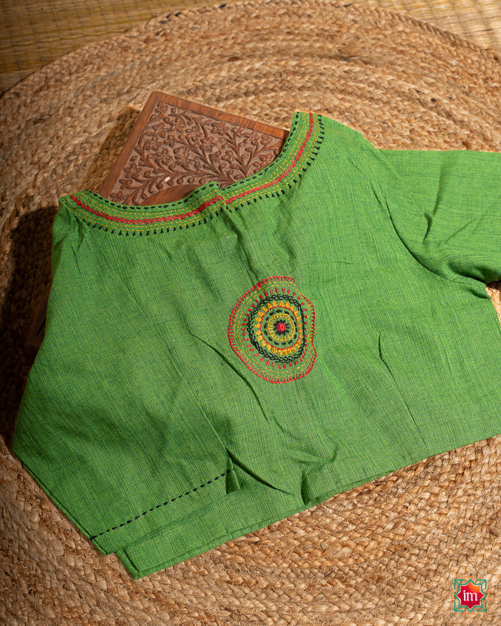 Beautiful back side green embroidery blouse which would suit any silk saree is kept upon a mat and a wooden designer box.