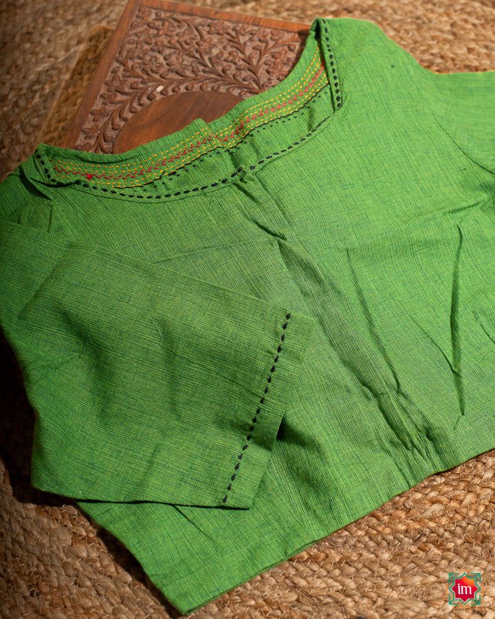 Beautiful green embroidery blouse which would suit any silk saree is kept upon a mat and a wooden designer box.