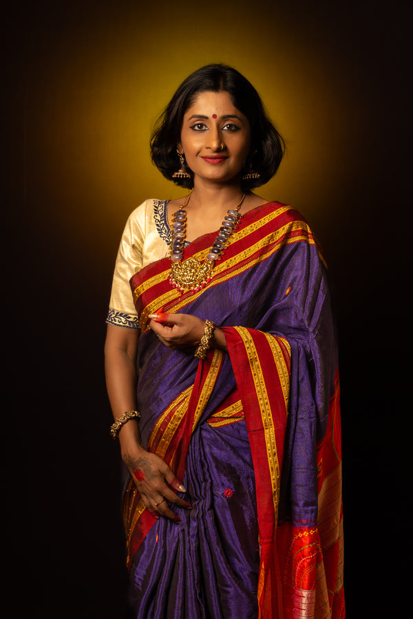 A women is dressed up and is posing by wearing beautiful purple saree with matching jewelry.