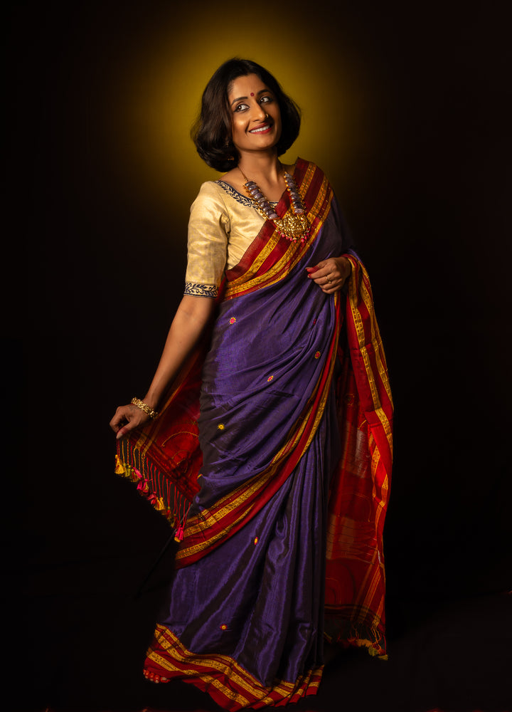 A women is dressed up and is posing by wearing beautiful purple saree with matching jewelry.
