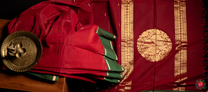 Beautiful red handloom saree is pleated and displayed upon a bench with a ganapati statue upon it.