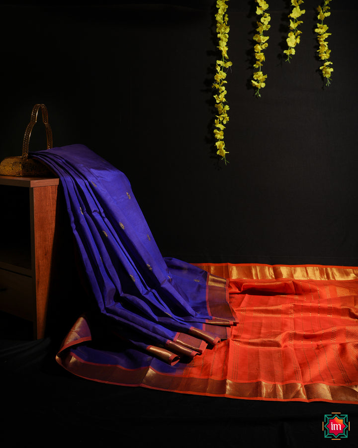 Beautiful Blue Kanchi Silk Saree is displayed on the floor with black background and yellow flowers hanging above.