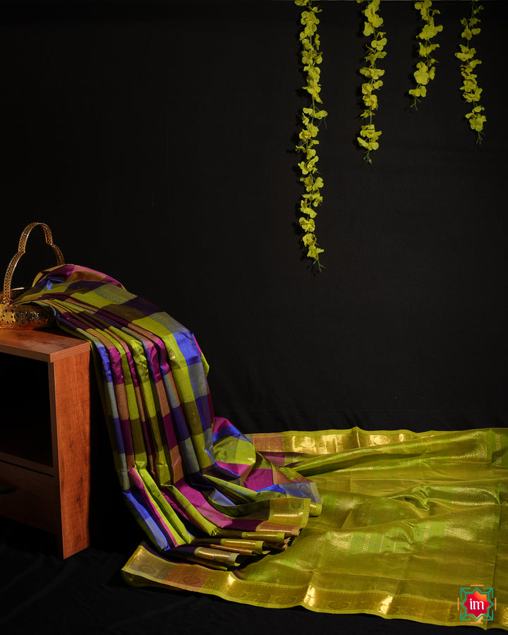Kanchi Silk Saree is displayed on the floor with black background and yellow flowers hanging above.