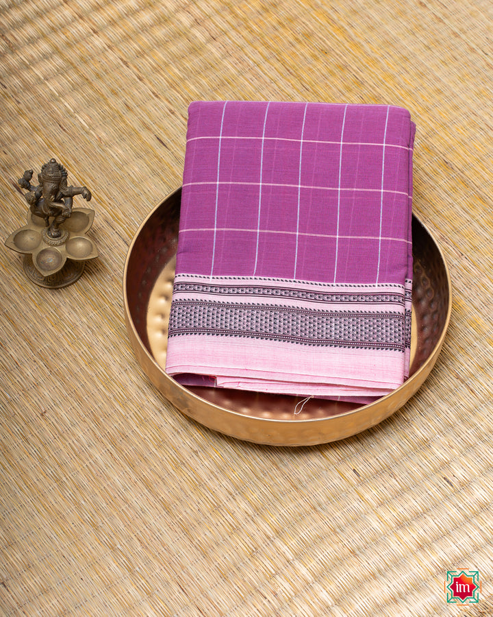 Beautiful orchid purple handloom cotton saree kept on a plate with ganapati statue beside which are kept upon the mat.