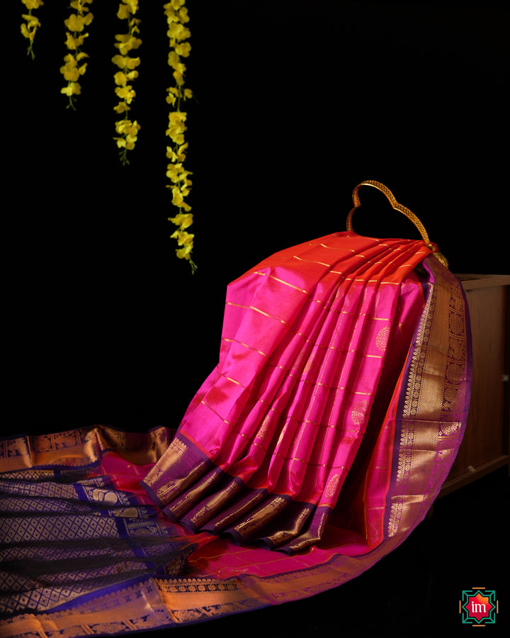 Elegant Candy Pink  Silk Saree is displayed on the floor with black background and yellow flowers hanging above.