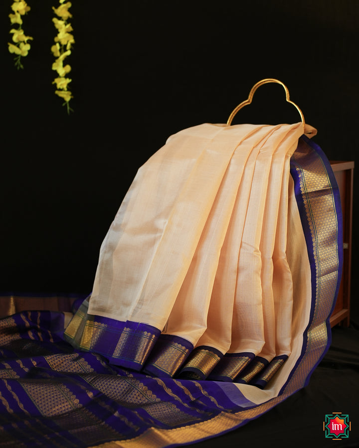 Beautiful Cream Kanchi Silk Cotton Saree best handloom cotton sarees for women is displayed on the floor with black background and yellow flowers hanging above.