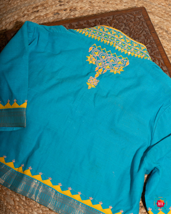 Elegant back side blue embroidery blouse which would suit any silk saree is kept upon a mat and a wooden designer box.