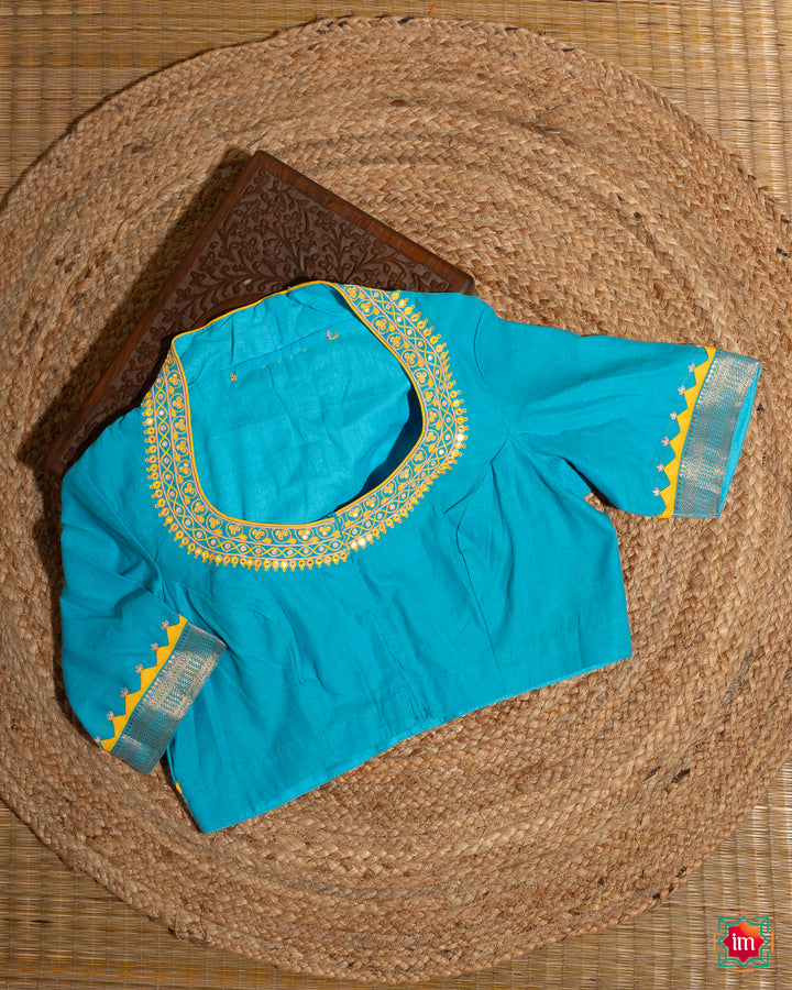 Elegant blue embroidery blouse which would suit any silk saree is kept upon a mat and a wooden designer box.