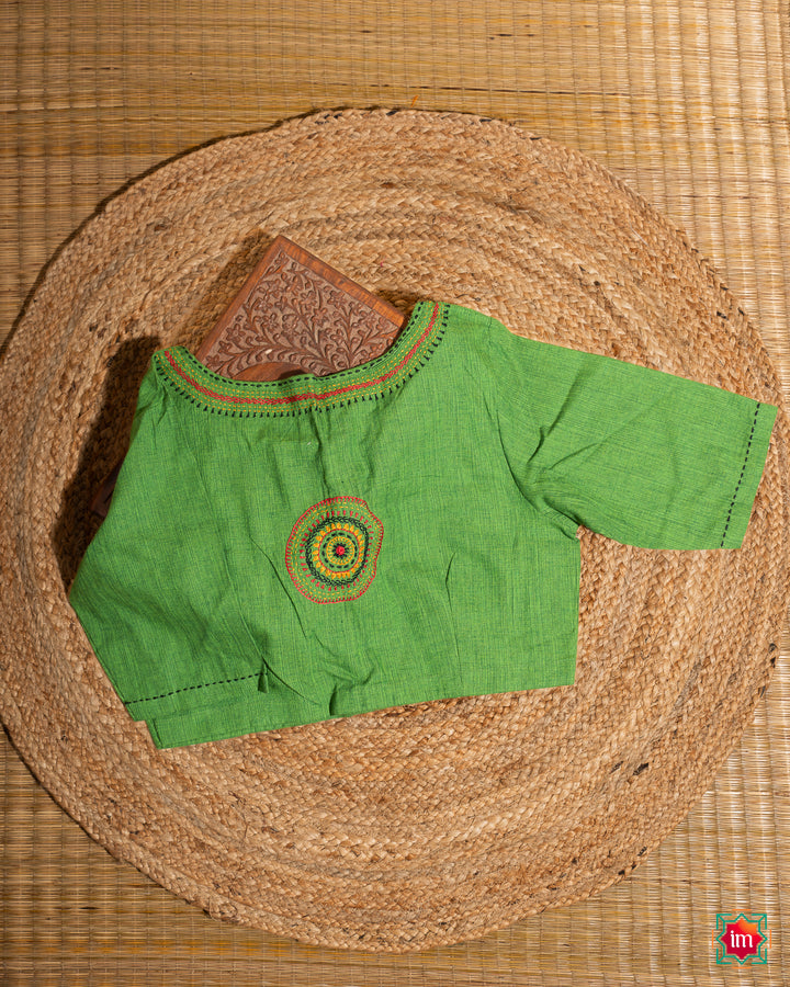 Beautiful back side green embroidery blouse which would suit any silk saree is kept upon a mat and a wooden designer box.