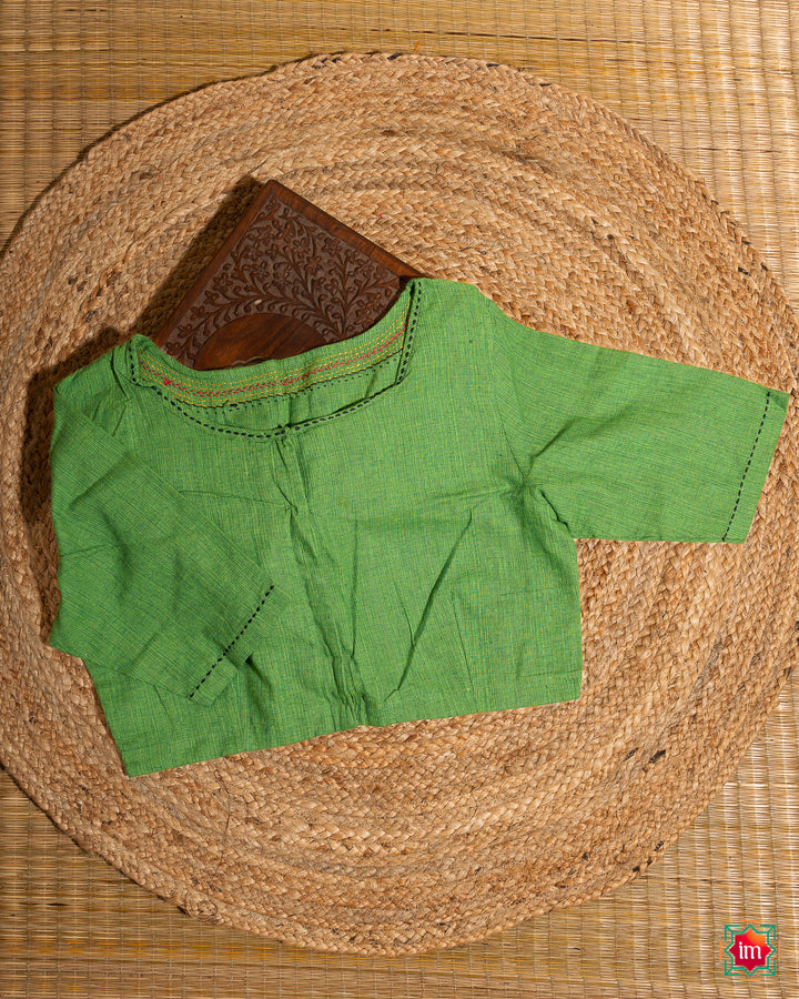 Beautiful green embroidery blouse which would suit any silk saree is kept upon a mat and a wooden designer box.