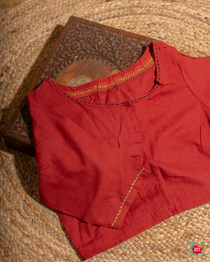 Beautiful red embroidery blouse which would suit any silk saree is kept upon a mat and a wooden designer box.