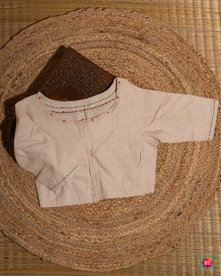 Elegant off-white embroidery blouse which would suit any silk saree is kept upon a mat and a wooden designer box.