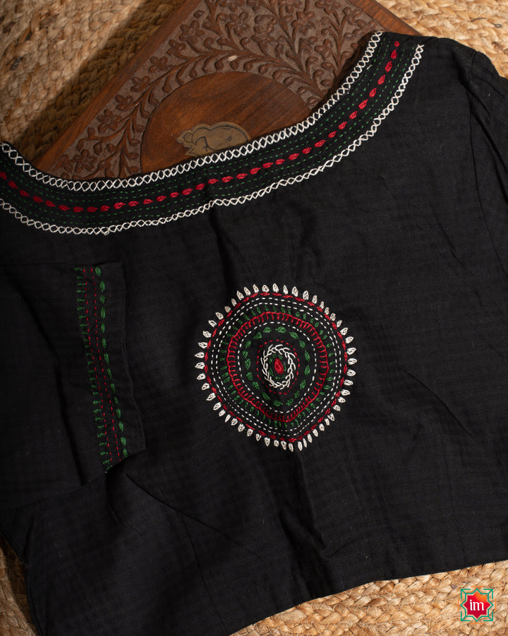 Beautiful back side black embroidery blouse which would suit any silk saree is kept upon a mat and a wooden designer box.