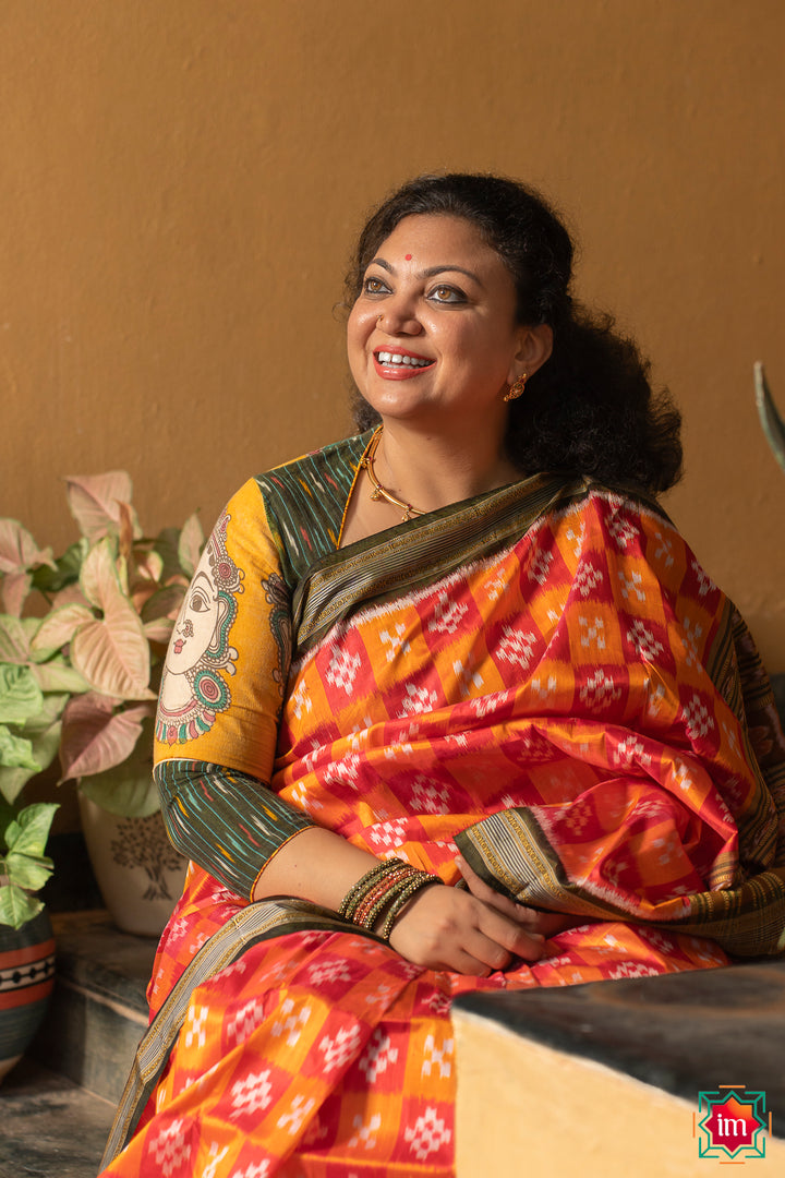 A women is dressed up and is posing outdoor by wearing beautiful red yellow silk saree with matching jewelry.