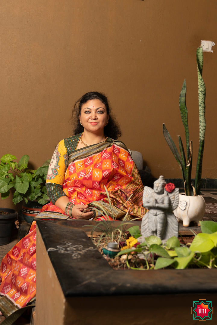 A women is dressed up and is posing outdoor by wearing beautiful red yellow silk saree with matching jewelry.