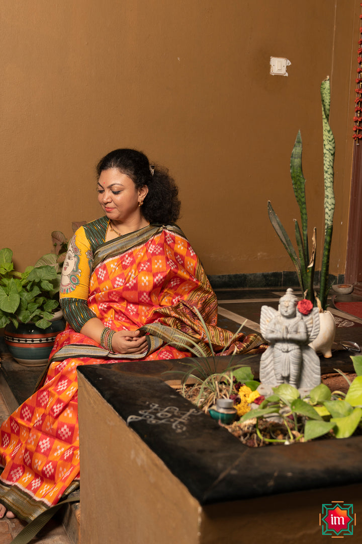 A women is dressed up and is posing outdoor by wearing beautiful red yellow silk saree with matching jewelry.