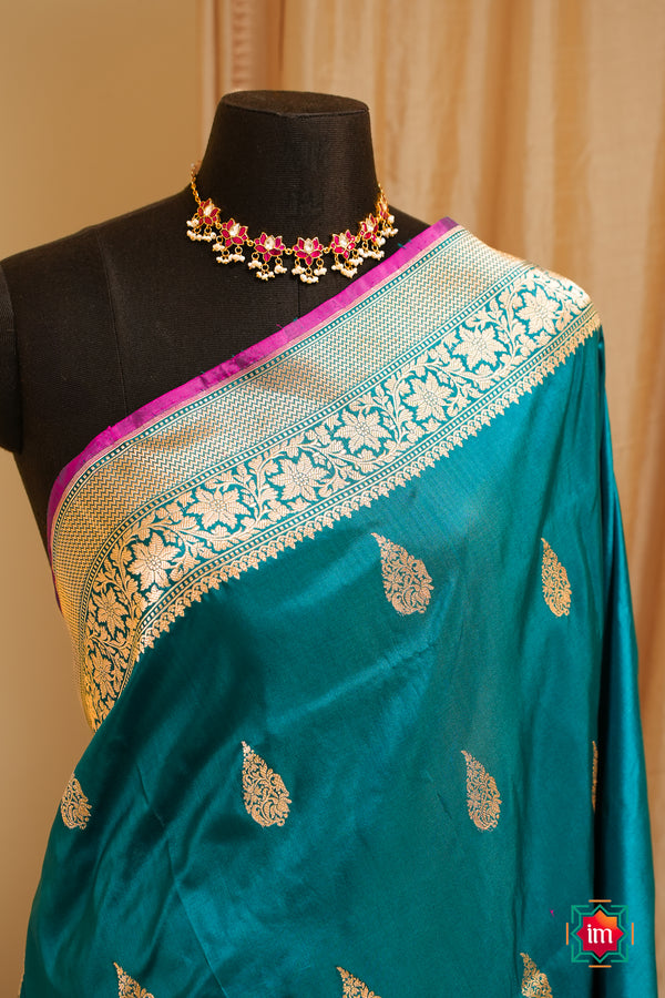 Teal banaras silk handloom saree with gold patterns on a mannequin against a beige curtain background
